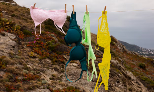 A vibrant bra dries outdoors, fluttering lightly in the fresh air against a backdrop of greenery.