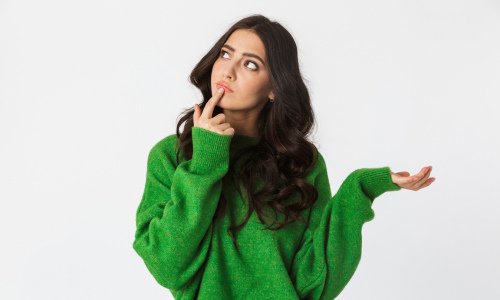 A woman in a green sweater and jeans gazes thoughtfully at an unseen object, her expression curious and engaged.