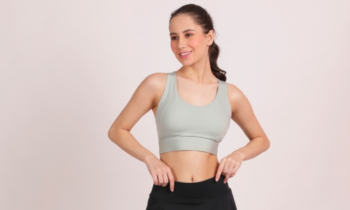 A confident woman in a medium impact sports bra with cross back flexing her muscles, showcasing her strength and fitness.